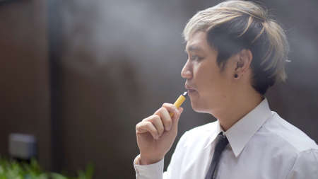 Asian white collar worker smoking an e-cigarette, alternative smoking for health.の写真素材