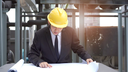 Professional Asian cilvil engineer reviewing and inspecting the building blue print at the construction site. Asian foreman working at the construction site on the building rooftop.の写真素材