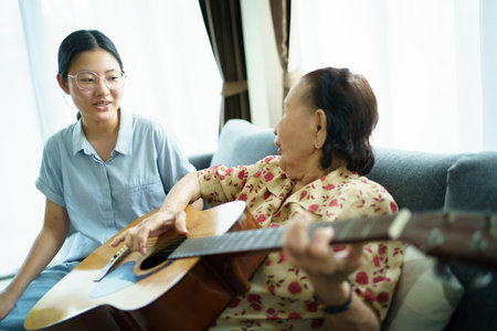 Asian elder woman playing an acoustic guitar and let her granddaughter taking a video on smartphone close up with copyspace. Elder Asian woman making a online video live streaming on social network.の写真素材
