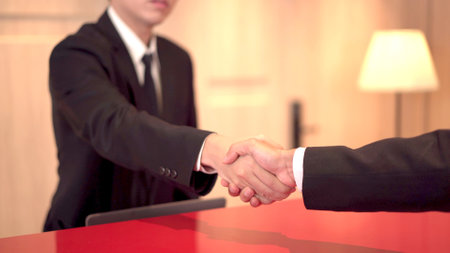 Asian young businessman making a handshake with hotel staff at the reception front desk. Business tourist customer greeting by making a hand shake to hotel reception officer.の写真素材