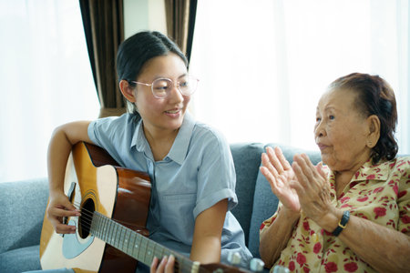 Asian elder woman playing an acoustic guitar and let her granddaughter taking a video on smartphone close up with copyspace. Elder Asian woman making a online video live streaming on social network.の写真素材