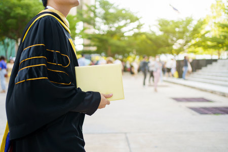 Happy Asian graduate student holding the diplomas on hand during the university graduation ceremony. Master degree student in gown suit holding a diplomas for photography.の写真素材