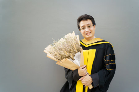 Happy Asian graduate student holding the diplomas on hand during the university graduation ceremony. Master degree student in gown suit holding a diplomas for photography.の写真素材