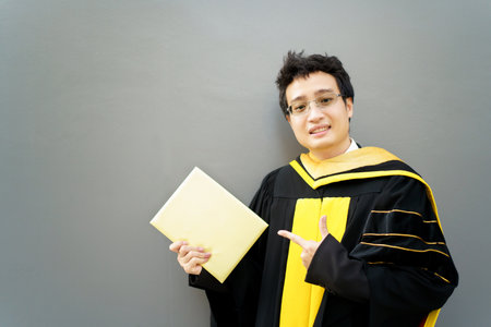 Happy Asian graduate student holding the diplomas on hand during the university graduation ceremony. Master degree student in gown suit holding a diplomas for photography.の写真素材