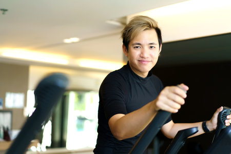 Active Asian young man making a cardio exercise on the elliptical exercise machine in the gym. Fat burn and body muscle building. bodybuilding workout concept.の写真素材