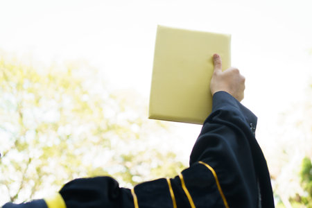 Happy Asian graduate student holding the diplomas on hand during the university graduation ceremony. Master degree student in gown suit holding a diplomas for photography.の写真素材