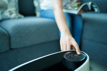 Happy Asian young woman turning on high efficiency air purifier while staying and reading a book in the living room. Woman using air purifier in her house.の写真素材