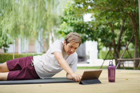 Active sportsman doing a plank exercise and making a video call with a friend and online sport training coach online. Healthy sport man making a body building workout with online instructor.の写真素材
