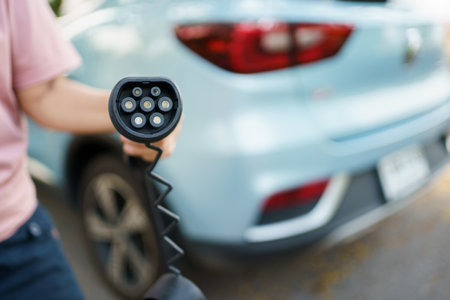 Unrecognizable Asian woman holding AC type 2 EV charging connector at EV charging station, woman preparing an EV - electric vehicle charging connector for recharge a vehicle.の写真素材