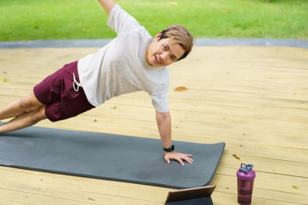 Active sportsman doing a side plank exercise and making a video call with a friend and online sport training coach. Healthy sport man making a body building workout with online instructor.の写真素材