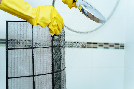 Asian woman cleaning a dirty and dusty air conditioning filter in her house. Housewife removing a...