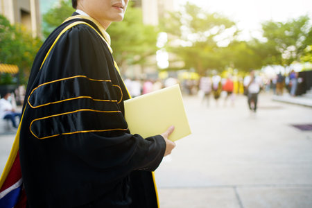 Happy Asian graduate student holding the diplomas on hand during the university graduation ceremony. Master degree student in gown suit holding a diplomas for photography.の写真素材