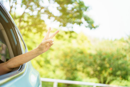 Unrecognizable Asian woman driver showing a thumb up outside the vehicle while driving a car. Happy woman driver or passenger showing her thumb up during in the car. Safety trip and freedom concept.の写真素材
