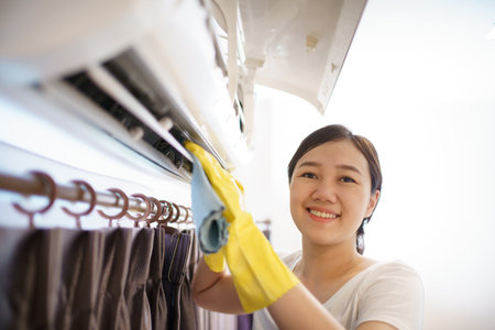 Asian woman cleaning a dirty and dusty air conditioning filter in her house. Housewife removing a dusty air conditioner filter.の写真素材