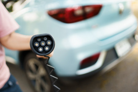 Unrecognizable Asian woman holding AC type 2 EV charging connector at EV charging station, woman preparing an EV - electric vehicle charging connector for recharge a vehicle.の写真素材