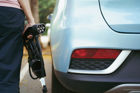 Unrecognizable woman holding the portable EV emergency charging adapter and preparing to charge the EV car. Electric Vehicle charging adapter close up with copyspace.の写真素材