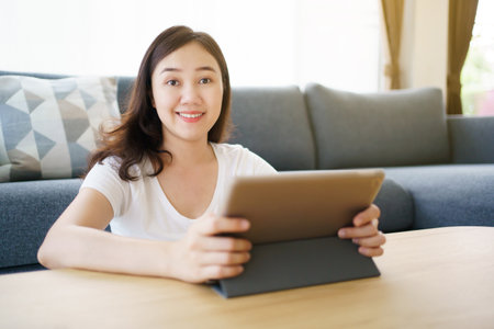 Happy Asian young woman relaxing in the living room and watching a contents and chatting with her friends and drawing an illustration on tablet. Woman enjoy watching video and drawing on tablet.の写真素材