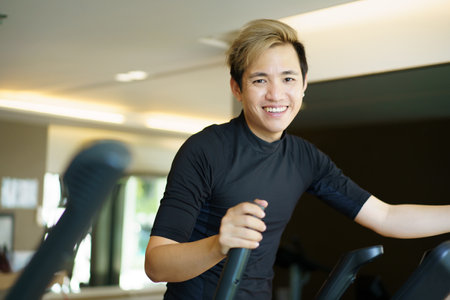 Active Asian young man making a cardio exercise on the elliptical exercise machine in the gym. Fat burn and body muscle building. bodybuilding workout concept.の写真素材