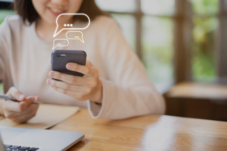 Unrecognizable cheerful young businesswoman reading a message on a smartphone close up. Asian girl working on a laptop computer and smartphone during staying at coffee shop. Online learning concept.の写真素材