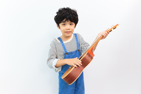 Happy Asian little boy enjoy practicing an acoustic guitar and smiling to camera for photography. Asian little boy holding a guitar.の写真素材