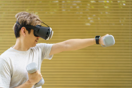 Active Asian sportsman doing a weight training exercise by using dumbbell and virtual reality - VR goggles platform for online training. The innovation of virtual reality or metaverse platform conceptの写真素材