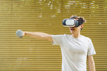 Active Asian sportsman doing a weight training exercise by using dumbbell and virtual reality - VR goggles platform for online training. The innovation of virtual reality or metaverse platform conceptの写真素材