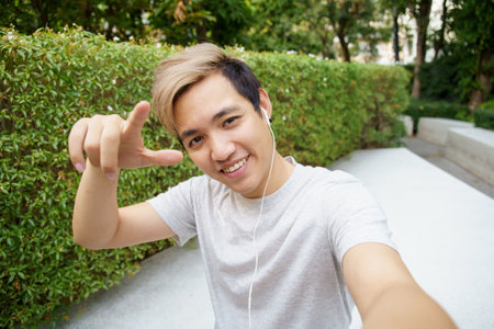Active happy Asian sportsman taking a self portrait photography or selfie on a smartphone while working out outdoor, Asian man takes selfies on smartphone. Sportsman having a video call on smartphone.の写真素材