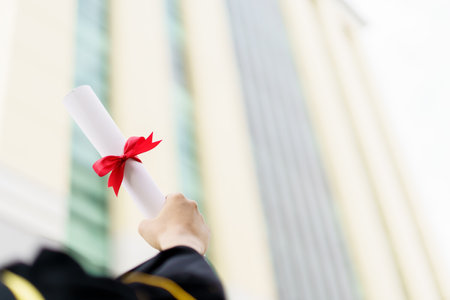 Happy Asian graduate student holding the diplomas on hand during the university graduation ceremony. Master degree student in gown suit holding a diplomas for photography.の写真素材