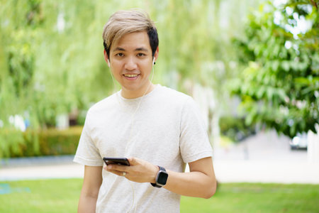 Handsome Asian young sportsman posing and smiling to the camera while his running exercise, man listening a music on smartphone while practicing running workout. Happy Asian athlete smiling.の写真素材