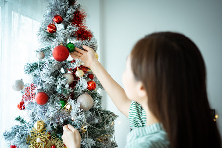 Happy Asian woman enjoy decorating a Christmas tree with a fantasy Christmas balls and presents. Happy beautiful woman preparing her residency or home for celebrating new year and Christmas party.の写真素材