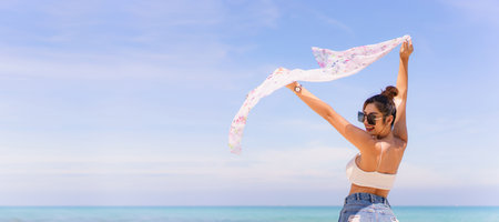 Beautiful Asian young woman in bikini enjoy walking and looking at the sea and beach in morning, woman rising a white scarf over her head.の写真素材