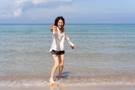 Happy Asian young woman enjoy playing and splashing a sea water at the beach. Summertime holiday and vacation concept. Cheerful Asian woman walking along the beach in morning and looking at camera.の写真素材