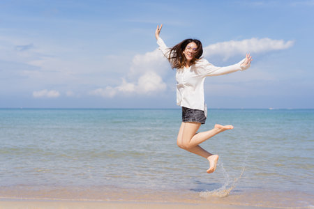 Happy Asian young woman enjoy playing and splashing a sea water at the beach. Summertime holiday and vacation concept. Cheerful Asian woman walking along the beach in morning and looking at camera.の写真素材