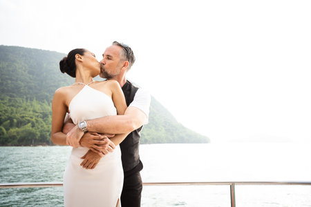Happy Asian and caucasian white couple celebrating their marriage anniversary together on the yacht. Adult couple sailing a yacht and drinking a Champaign together during a honeymoon trip.の写真素材