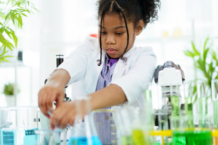 Lovely school girl excited to do a science experiment in science laboratory classroom. Hispanic - black ethnic girl dropping a liquid sampling into the experimental tube.の写真素材