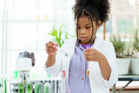 Lovely school girl excited to do a science experiment in science laboratory classroom. Hispanic - black ethnic girl dropping a liquid sampling into the experimental tube.の写真素材