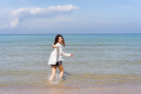 Happy Asian young woman enjoy playing and splashing a sea water at the beach. Summertime holiday and vacation concept. Cheerful Asian woman walking along the beach in morning and looking at camera.の写真素材