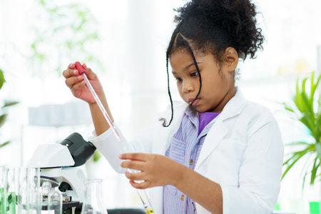 Lovely school girl excited to do a science experiment in science laboratory classroom. Hispanic - black ethnic girl dropping a liquid sampling into the experimental tube.の写真素材