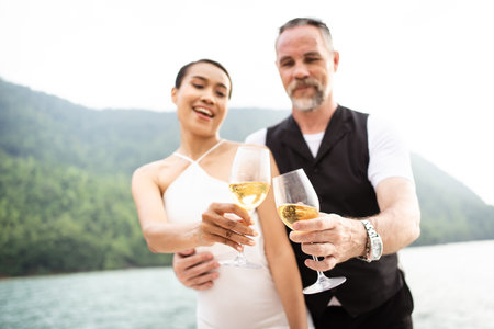 Happy Asian and caucasian white couple celebrating their marriage anniversary together on the yacht. Adult couple sailing a yacht and drinking a Champaign together during a honeymoon trip.の写真素材