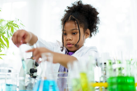 Lovely school girl excited to do a science experiment in science laboratory classroom. Hispanic - black ethnic girl dropping a liquid sampling into the experimental tube.の写真素材