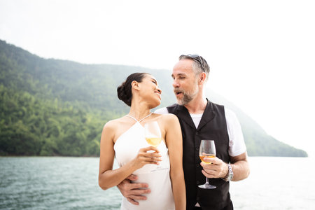 Happy Asian and caucasian white couple celebrating their marriage anniversary together on the yacht. Adult couple sailing a yacht and drinking a Champaign together during a honeymoon trip.の写真素材
