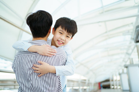 Happy cheerful Asian little boy running to his father at the railway or sky train station after his father returned from the traveling trip. Happy Asian family father and son concept.の写真素材