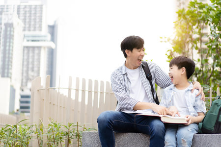 Cheerful happy Asian little boy and his father reading a book or fairy tale together at the outdoor park. Asian man and his son reading a book together.の写真素材