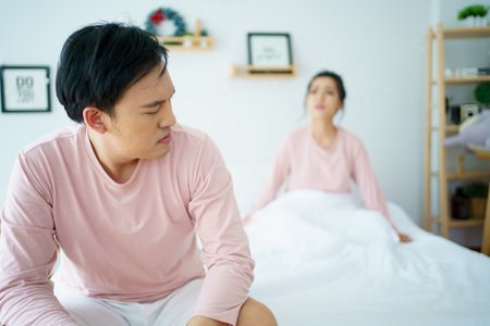 Unhappy - stressful Asian man sitting on the bed while his wife shouting at him. Critical or serious arguing between husband and wife about a problem in family.の写真素材