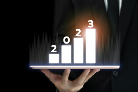 Unrecognizable businessman holding a digital tablet and showing a business chart or bar graph with a year 2023 in hologram with copy space. A successful and growth in business in 2023 concept.の写真素材