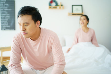 Unhappy - stressful Asian man sitting on the bed while his wife shouting at him. Critical or serious arguing between husband and wife about a problem in family.の写真素材