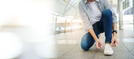 Asian young man sitting on the ground and tie a shoelaces with copyspace. A Man traveling in the city or downtown and tying a shoelaceの写真素材