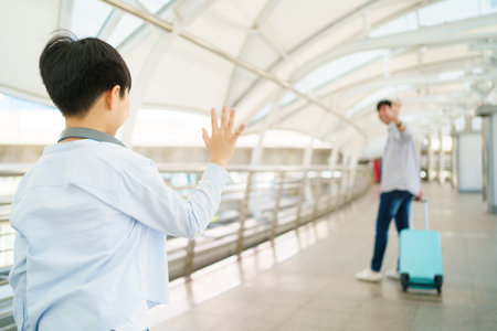 Asian little boy waves a hand and says goodbye to his father at the airport or railway terminal before father leaving.の写真素材