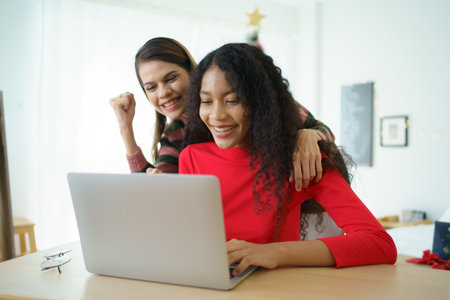 Caucasian white and African black ethnic women using laptop - notebook computer and having a discussion together in the room. Young woman colleagues working together on laptop computer.の写真素材