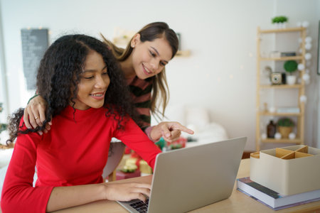 Caucasian white and African black ethnic women using laptop - notebook computer and having a discussion together in the room. Young woman colleagues working together on laptop computer.の写真素材